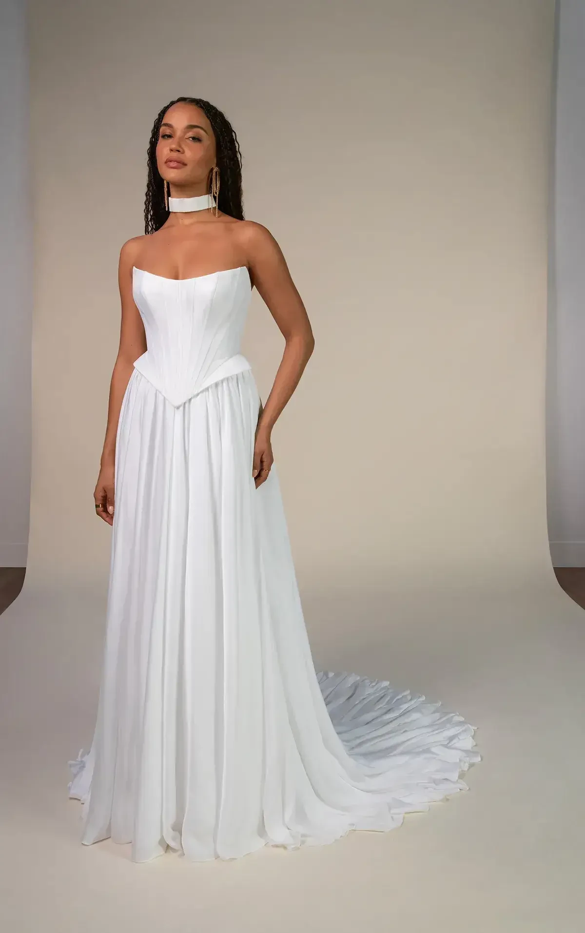 A person wearing a strapless white gown with a long train, standing against a neutral background.