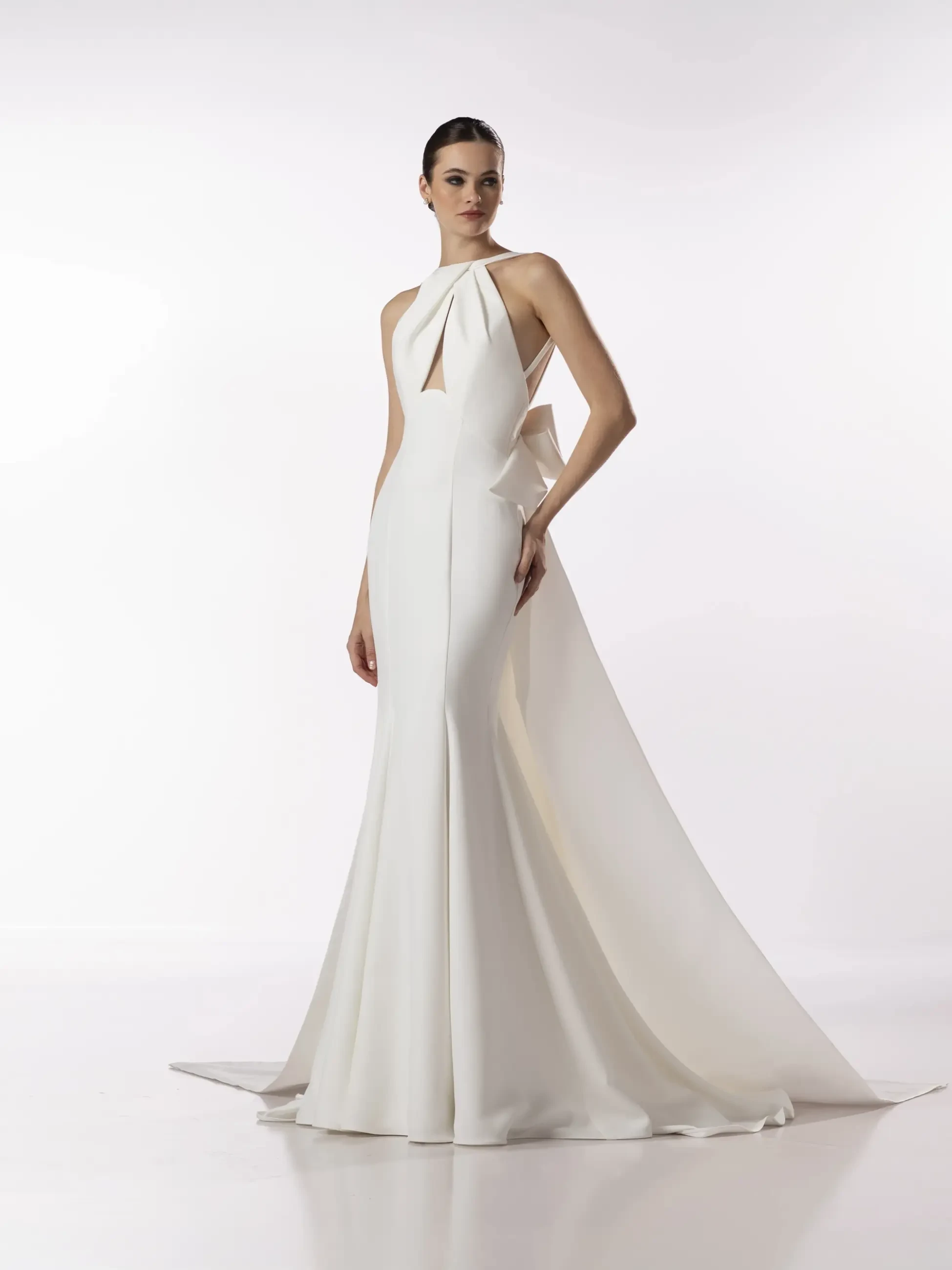 Elegant model in a sleek, floor-length white gown with a halter-neck and flowing train. The setting is bright, conveying a sophisticated and graceful tone.
