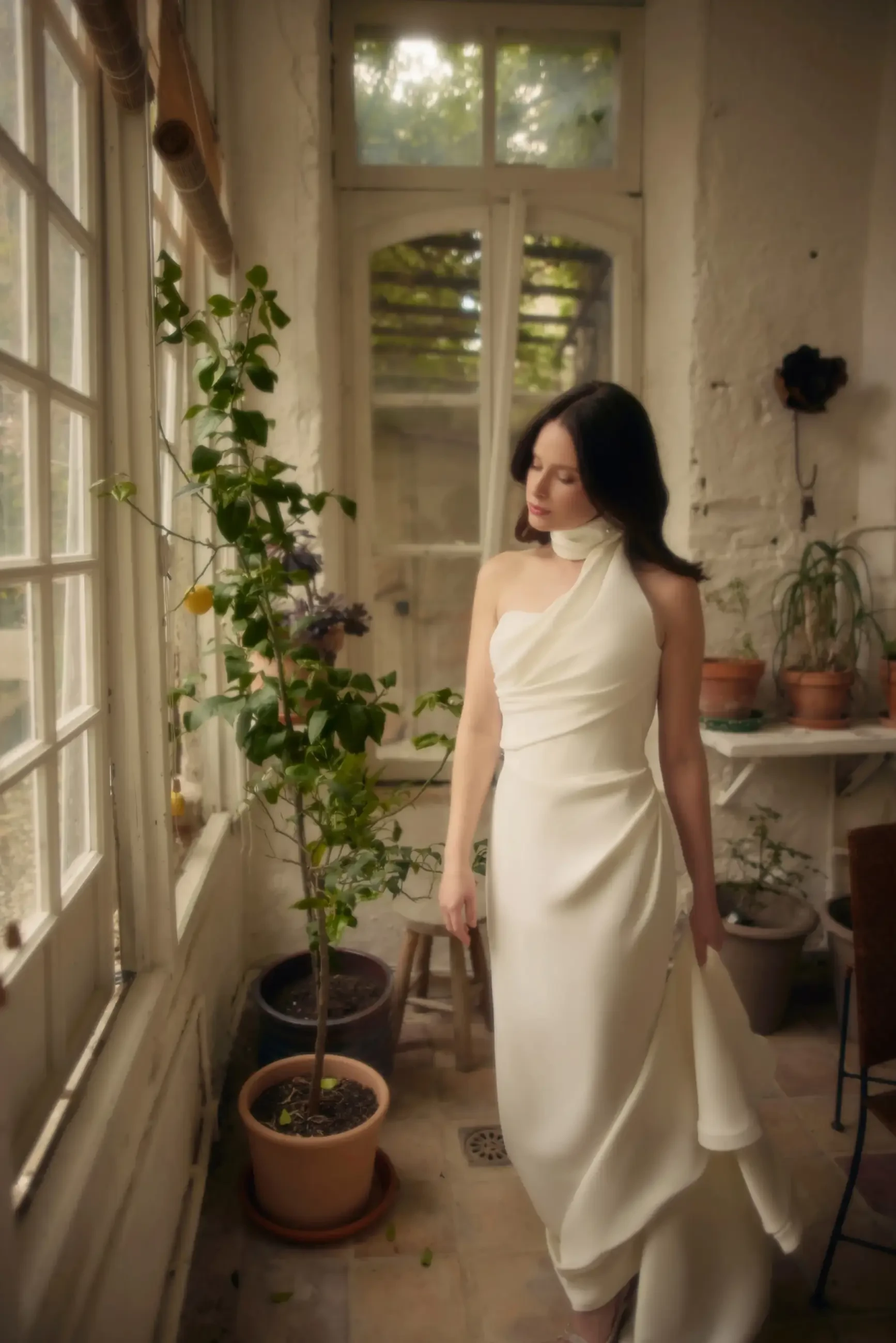 Model is wearing a column wedding dress with an asymmetrical neckline