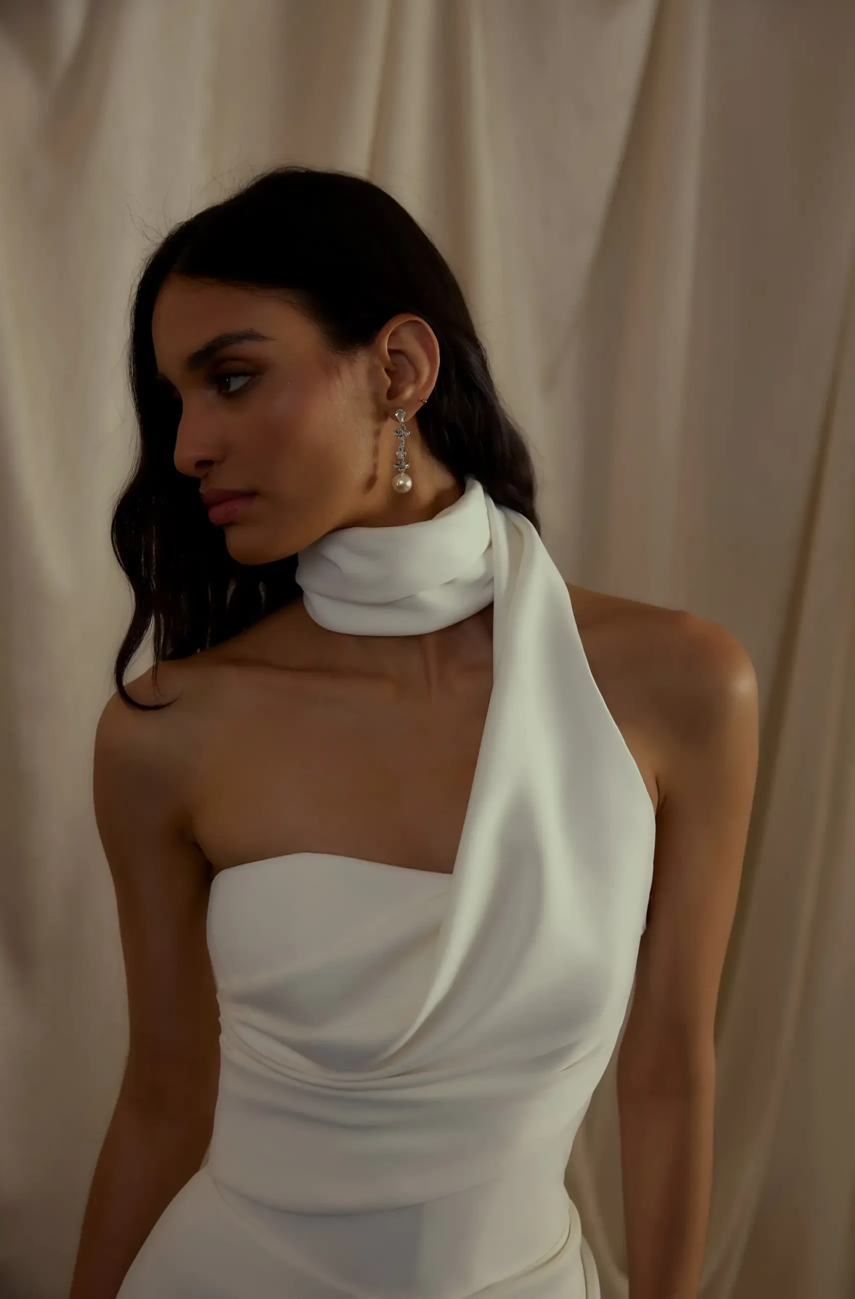 Model is wearing a column wedding dress with an asymmetrical neckline