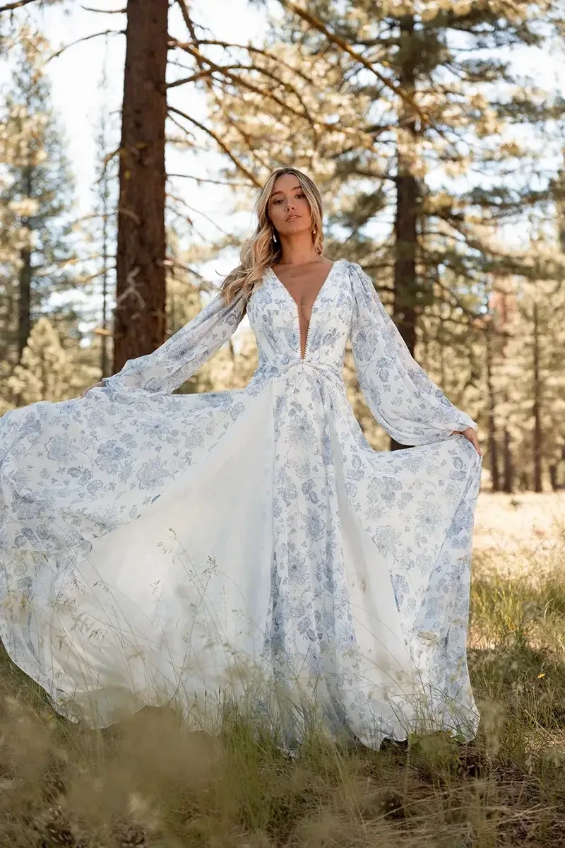 Model is wearing a boho A-line wedding dress with a deep V-neckline, detachable long blouson sleeves, paisley print panels, belted waist, and flowing chiffon skirt.
